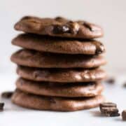 Dark Chocolate Chunk paleo cookies stacked on top of each other, setting next to dark chocolate morsels.