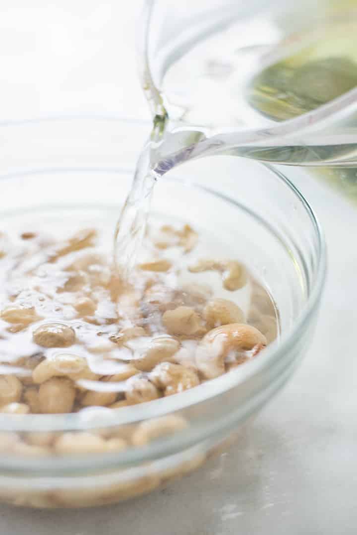 Bowl of raw cashews with boiling hot water being poured over them in order to soak and soften to be used in the cashew lime crema for the chicken protein bowl.