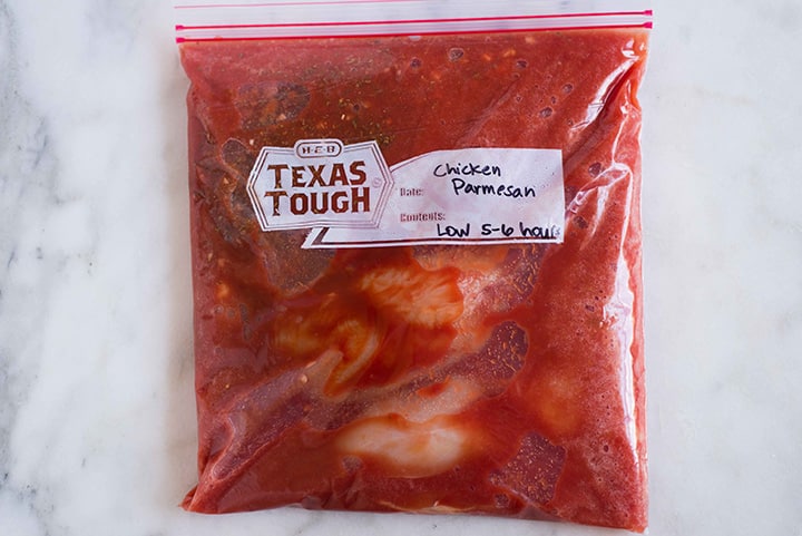 Large ziploc bag filled with contents for slow cooker chicken parmesan that will be frozen and then cooked in a crock pot.