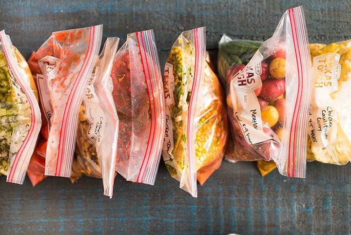 Line of slow cooker freezer meals filled in large ziploc bags, including slow cooker chicken parmesan, chicken cauliflower curry, split pea soup, meatloaf, chicken tortilla soup, and cashew chicken.