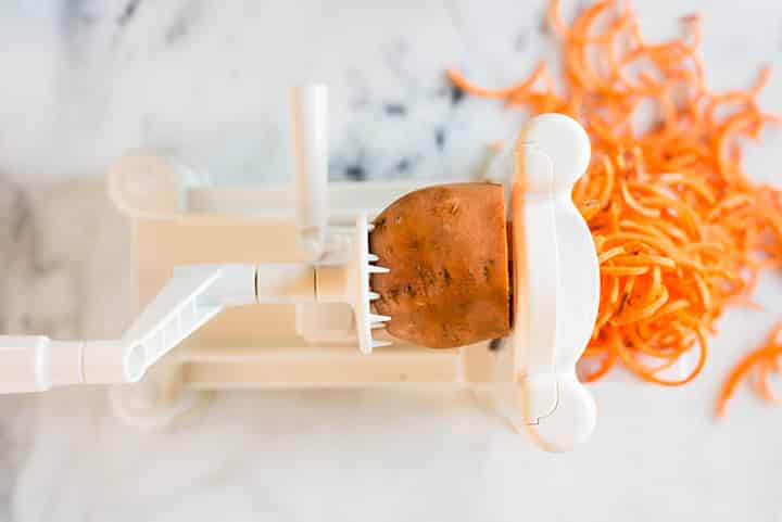 Overhead view of a sweet potato being spiralized to show how to spiralize sweet potato.