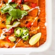 Close up image of a white casserole dish filled with vegan enchiladas made with quinoa and black beans, and topped with cilantro and avocado.