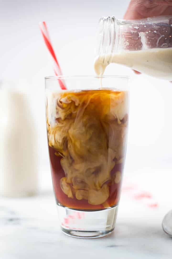 Pouring the healthy homemade coffee creamer into a glass filled with iced coffee.