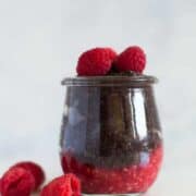 Jar of dark chocolate chia pudding which is layered over fresh mashed raspberries and topped with raspberries for the chia pudding recipe.