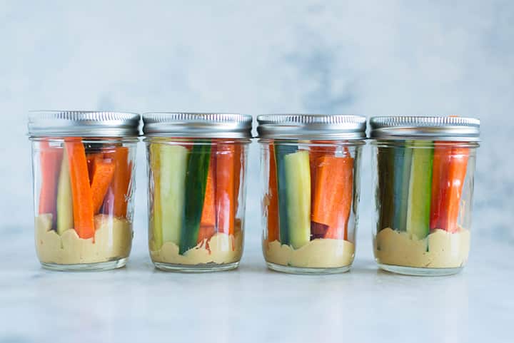 View of one of the snacks for the meal plan for weight loss, which is hummus topped with carrot stick and cucumber sticks, stacked in a mason jar.