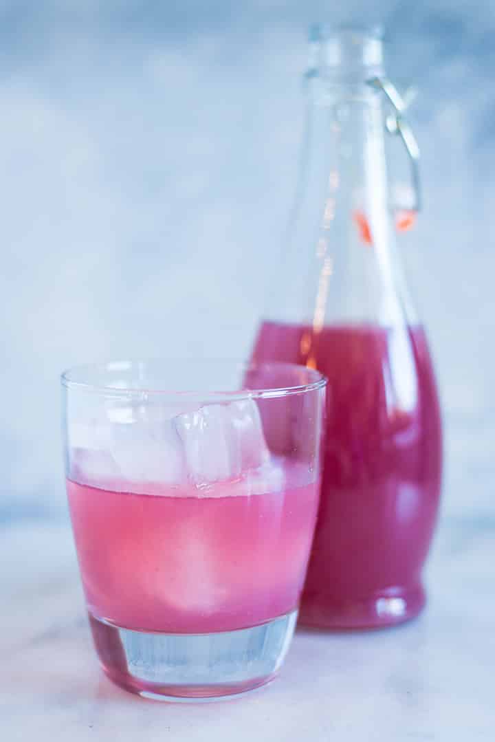A close up of a glass of Caffeine-free Homemade Grape Soda made from fresh grapes, raw honey simple syrup and seltzer water, served with ice cubes.