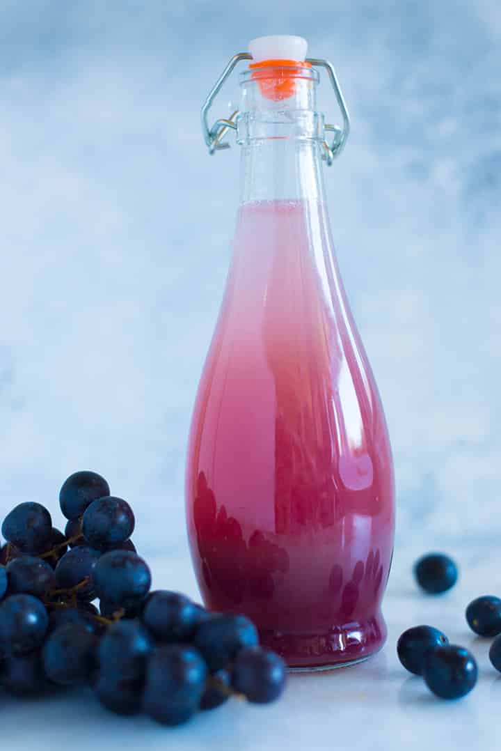 A side image of a sealed glass bottle with Caffeine-free Homemade Grape Soda made from fresh grapes, raw honey simple syrup and seltzer water.