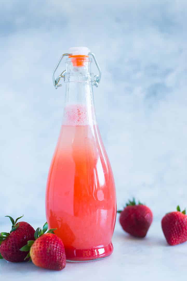 A side image of a sealed glass bottle with Caffeine-free Homemade Strawberry Soda made with fresh strawberries, raw honey simple syrup and seltzer water.