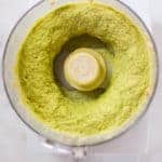 An overhead image of a food processor with Avocado Hummus made from avocado, canned chickpeas, olive oil, tahini, garlic, cumin, fresh lime juice, salt and ground black pepper.