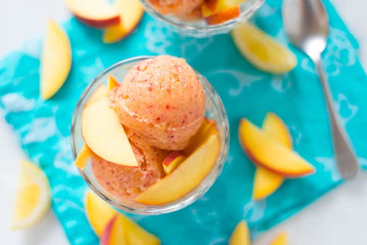 An overhead image of a glass dessert cup with two scoops of Peach Sorbet decorated with fresh peach slices.