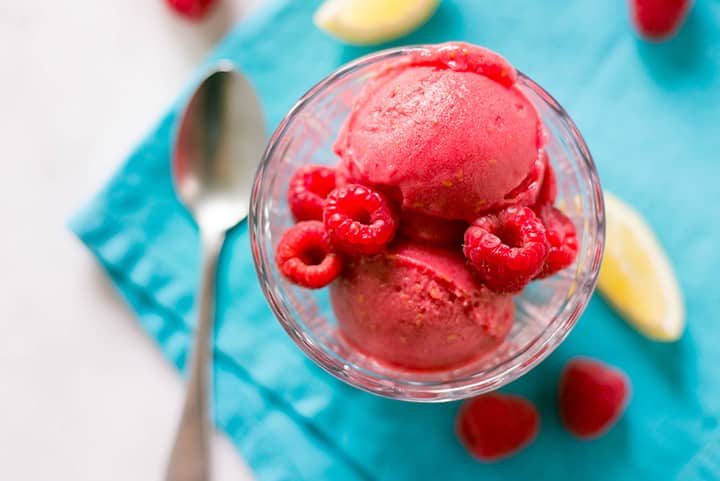A close up of two scoops of fresh Raspberry sorbet in a glass decorated with whole fresh raspberries.