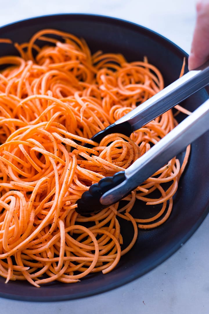 A side image of cooking the spiralized sweet potato noodles in a large skillet with olive oil.