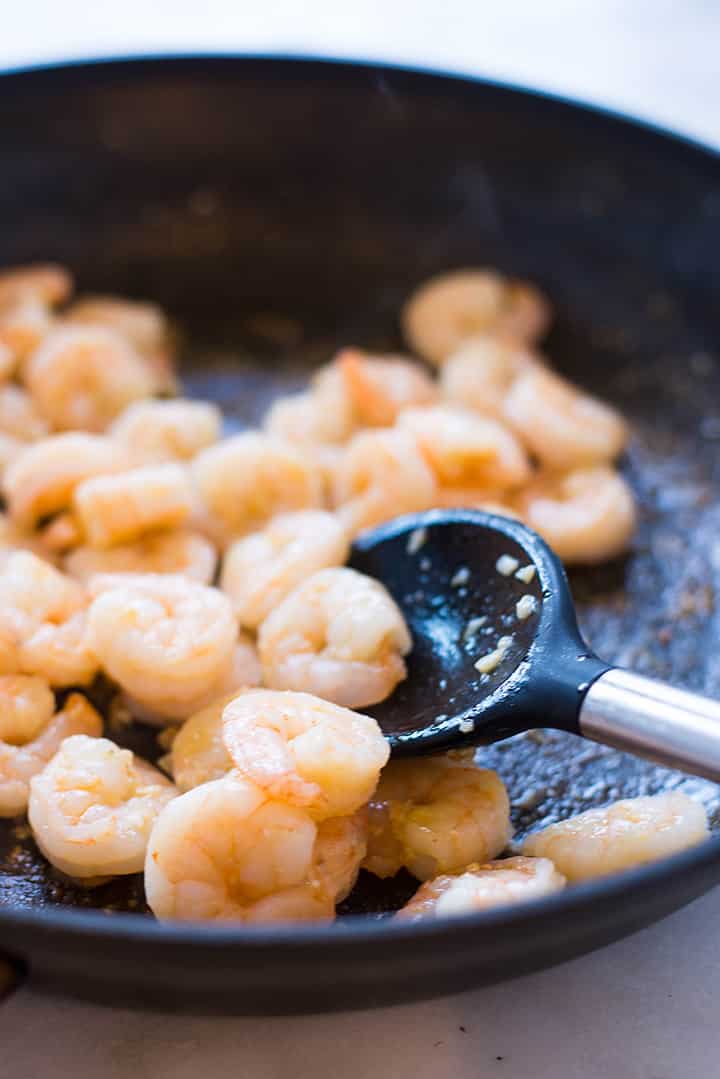 A side image of cooking shrimp with garlic in a large skillet for the Creamy Tuscan Shrimp With Sweet Potato Noodles.