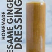 A single glass container holding Sesame Ginger Dressing as an example of Healthy Salad Dressing, which is next to the fresh ginger root.