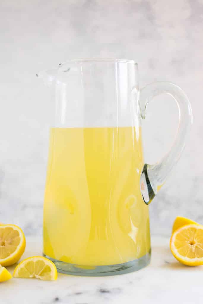 A side image of a pitcher on a kitchen counter half-filled with the basic Homemade Lemonade made with freshly squeezed lemon juice, water and raw honey.