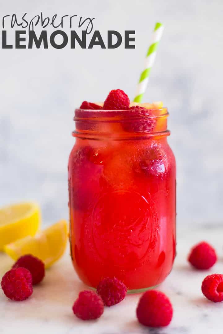 A side image of a mason jar filled with Easy Homemade Raspberry Lemonade, made from fresh raspberries, freshly squeezed lemon juice, water and raw honey, served with a slice of lemon, fresh raspberries and ice cubes.