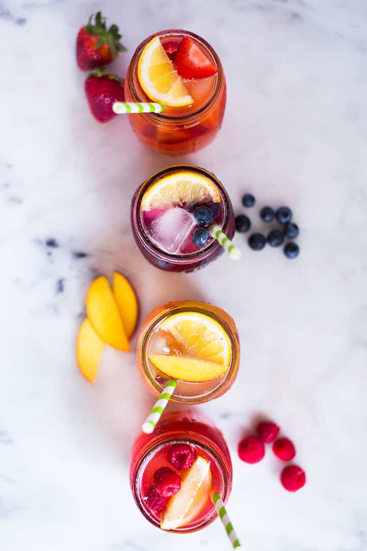 An overhead image of four mason jars on the kitchen counter each filled with Easy Homemade Lemonade including Strawberry Lemonade, Blueberry Lemonade, Peach Lemonade and Raspberry Lemonade, which include lemons, a citrus fruit to lower blood sugar.