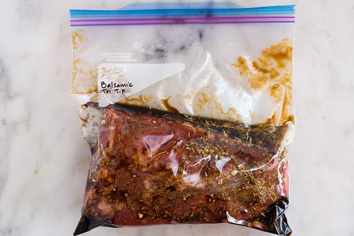 An overhead image of a sealable freezer bag with a tip tip steak in the Balsamic Tri Tip Marinade with reduced sodium soy sauce, balsamic vinegar, olive oil, crushed garlic cloves, rosemary and ground black pepper.