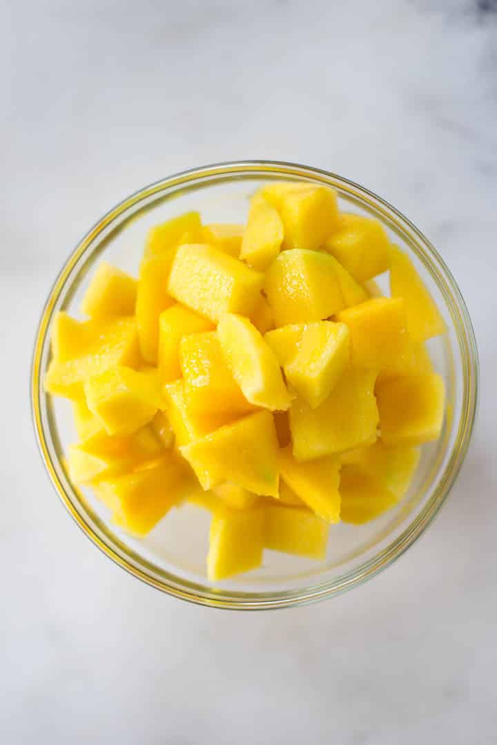An overhead image of a glass bowl with fresh diced mango ready to be frozen and then blended into Mango Sorbet.