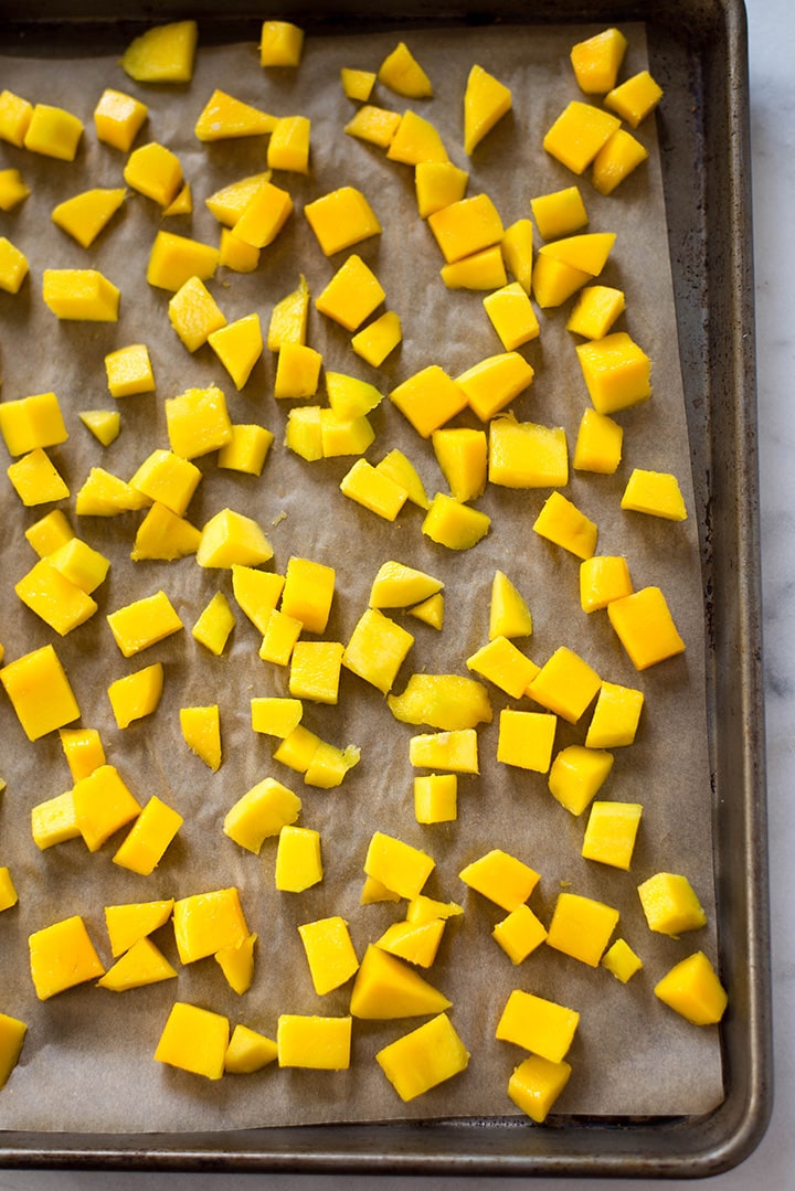An overhead image of diced mango laid out on a rimmed baking sheet covered with parchment paper ready to be frozen for the Mango Sorbet.