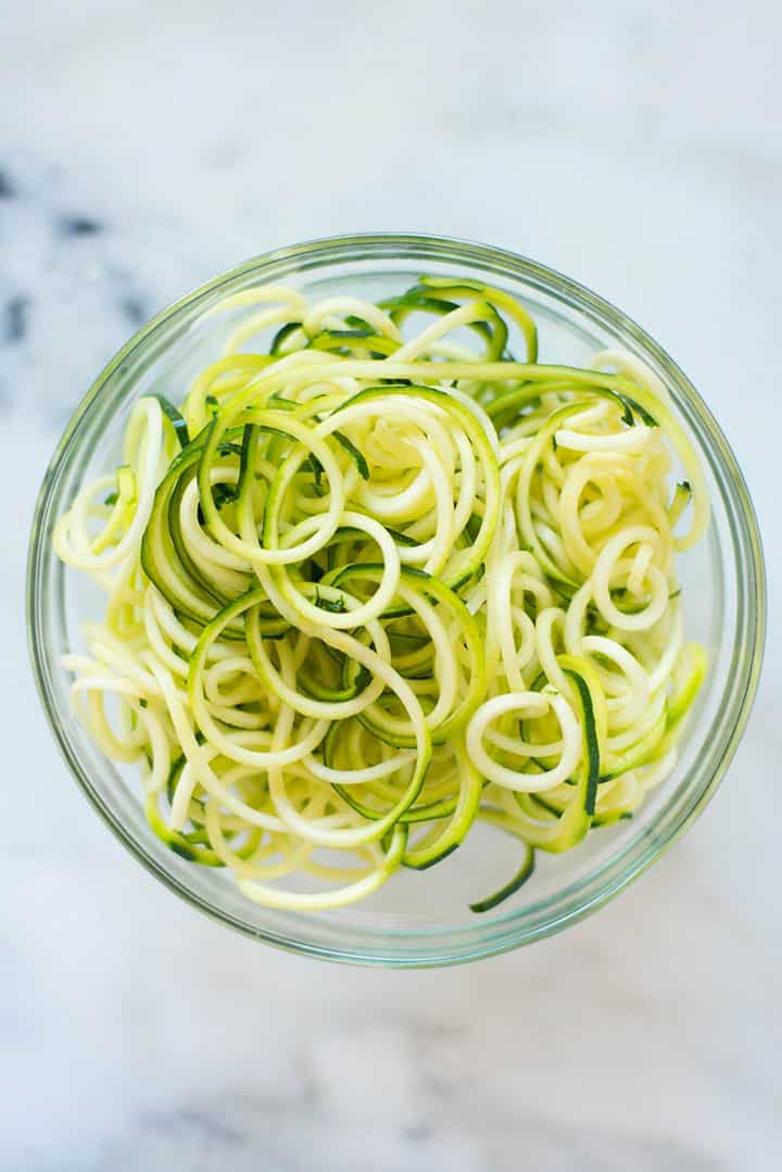 An overhead image of a glass bowl with fresh spiralized zucchini noodles ready to be cooked and served with Healthy Chicken Parmesan.