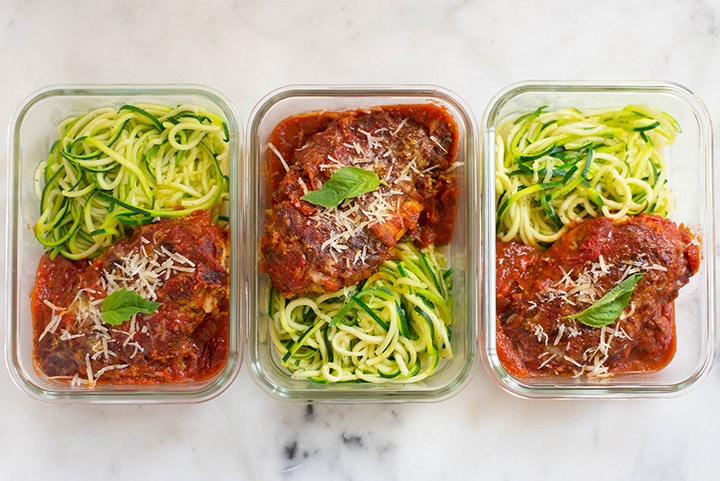 An overhead image of three glass containers lined up on a kitchen counter each with a single serving of Healthy Chicken Parmesan served with zucchini noodles ready to be placed in the refrigerator for meal prep.