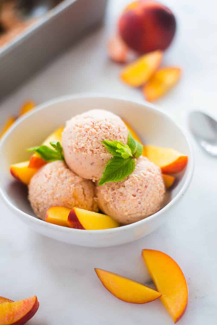 A side image of a serving of Peach Ice Cream made with ripe peaches, full-fat coconut milk, vanilla extract, maple syrup, lemon juice and cinnamon, served with fresh peach slices.