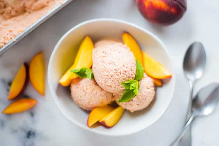 A close up image of three scoops of freshly made Peach Ice Cream, made with ripe peaches, full-fat coconut milk, vanilla extract, maple syrup, lemon juice and cinnamon, served with fresh peach slices.