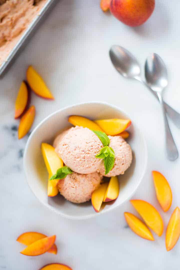 An overhead image of a serving of freshly made Peach Ice Cream in a dessert bowl on a kitchen counter, served with fresh peach slices.