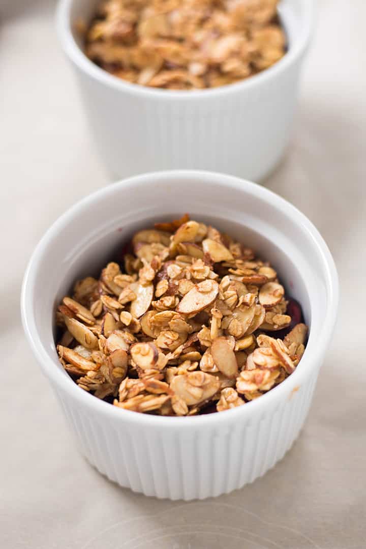 A close up image of a ramekin with Fresh and Healthy Cherry Crisp made with cherries, pure maple syrup, arrowroot starch, lemon juice, sea salt, sliced almonds, rolled oats, coconut oil and ground cinnamon ready for the oven.