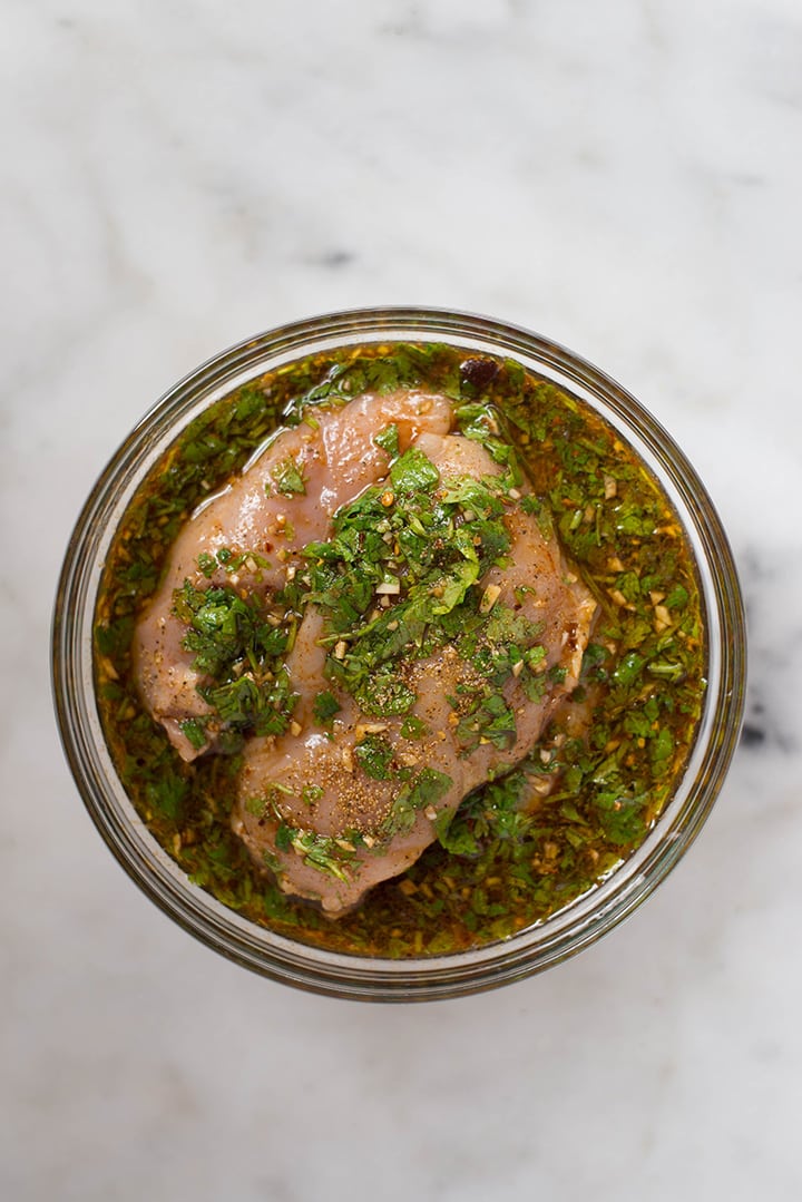 An overhead image of skinless, boneless chicken breasts in a marinade of lime juice, pineapple juice, low sodium soy sauce, garlic, ground cumin, paprika, red pepper flakes, cilantro, olive oil, sea salt and ground black pepper for the Healthy Chicken Fajitas.