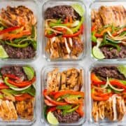 A side image of 6 meal prep containers with Healthy Chicken Fajitas, made with Fajita Chicken, Fajita Bell Peppers and Lime & Cilantro Black Beans stored in the fridge.