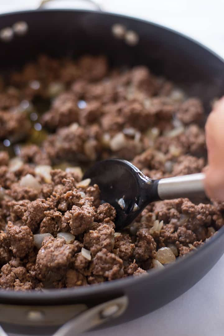 A close up image of a spoon stirring ground beef and garlic in a large skillet for the Homemade Chili.