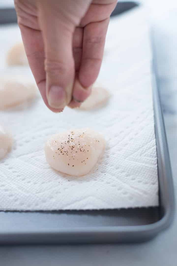Close-up of seasoning scallops on a paper towel before searing them.