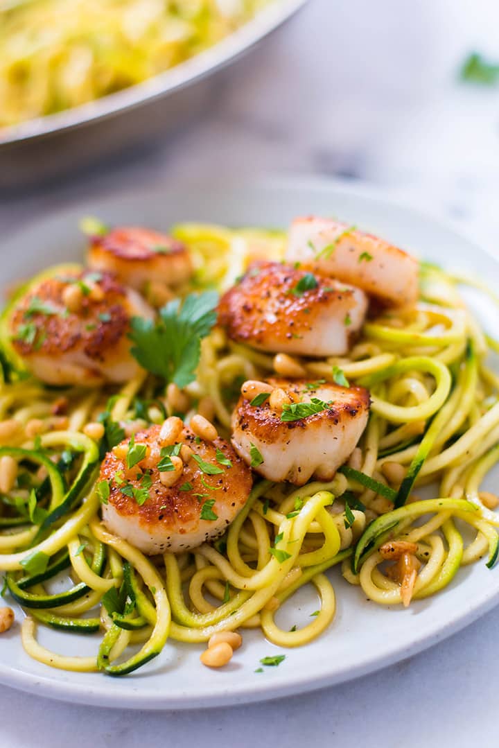 Overhead view of a white plate with pan-seared scallops on a bed of zucchini noodles.