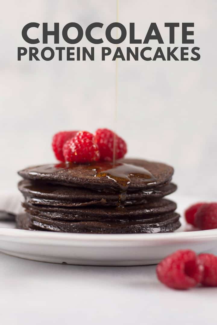 A side image of a stack of Chocolate Protein Pancakes made with eggs, ripe bananas, uncooked rolled oats, chocolate protein powder, unsweetened cocoa powder and ground cinnamon, topped with fresh raspberries and drizzled with pure maple syrup.