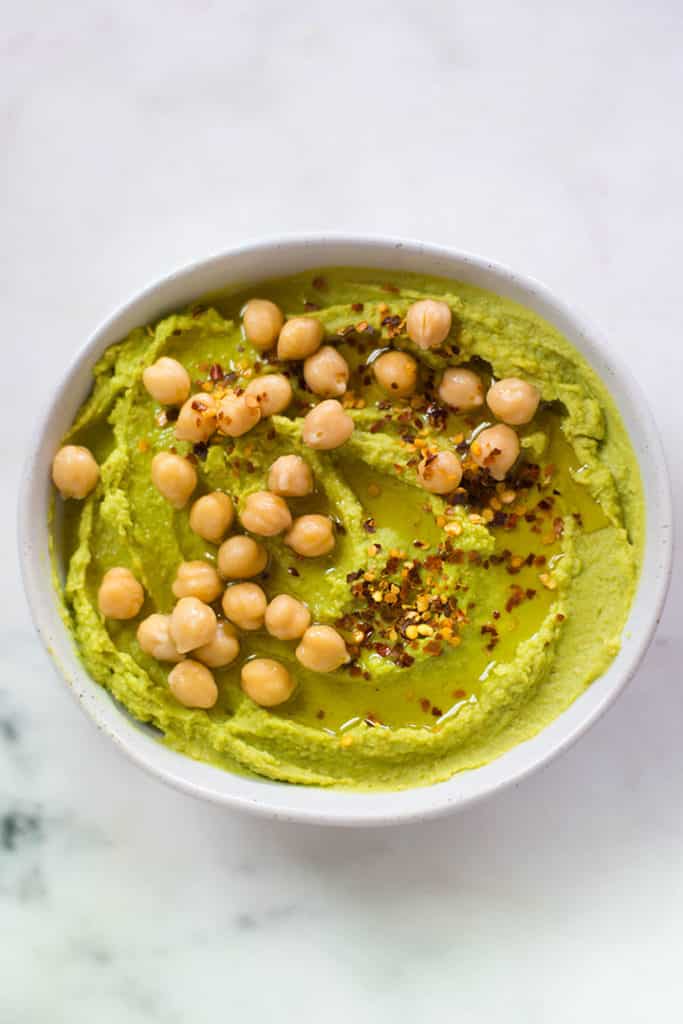 Overhead image of a white bowl containing avocado hummus, a food to fight belly fat.