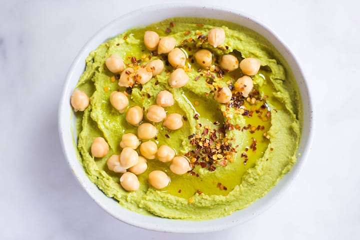 Close up of Healthy Avocado Hummus garnished with chickpeas and red pepper flakes.