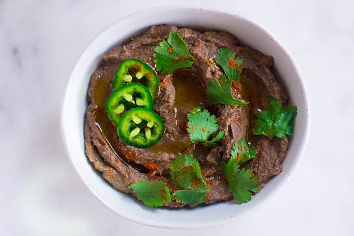 Healthy Black Bean Hummus garnished with cilantro, jalapeno, and cayenne pepper in a bowl ready to be served.