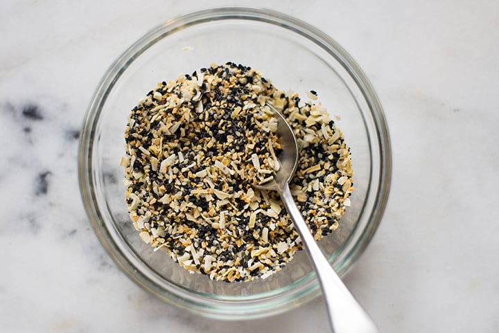 An overhead image of a kitchen counter with a bowl of Homemade Everything Bagel Seasoning made with black sesame seeds, white sesame seeds, flaked sea salt, dried onion flakes, poppy seeds and dried minced garlic.