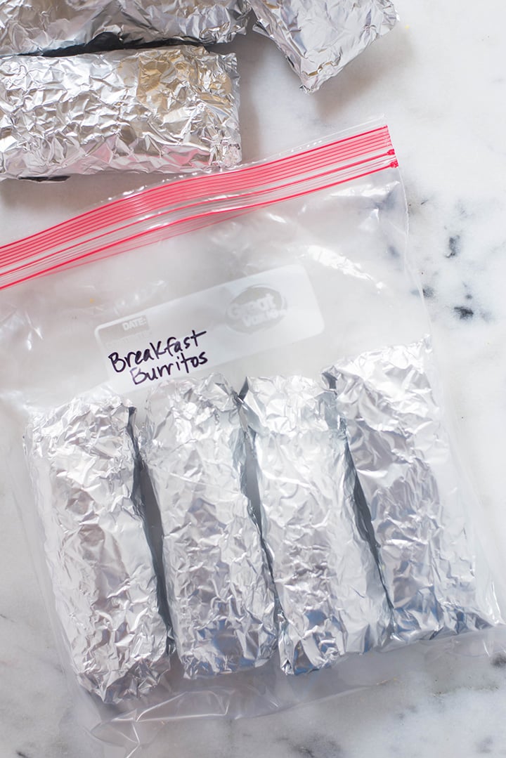 Breakfast burritos covered in aluminum foil placed in a freezer safe bag, ready to be stored in the freezer.