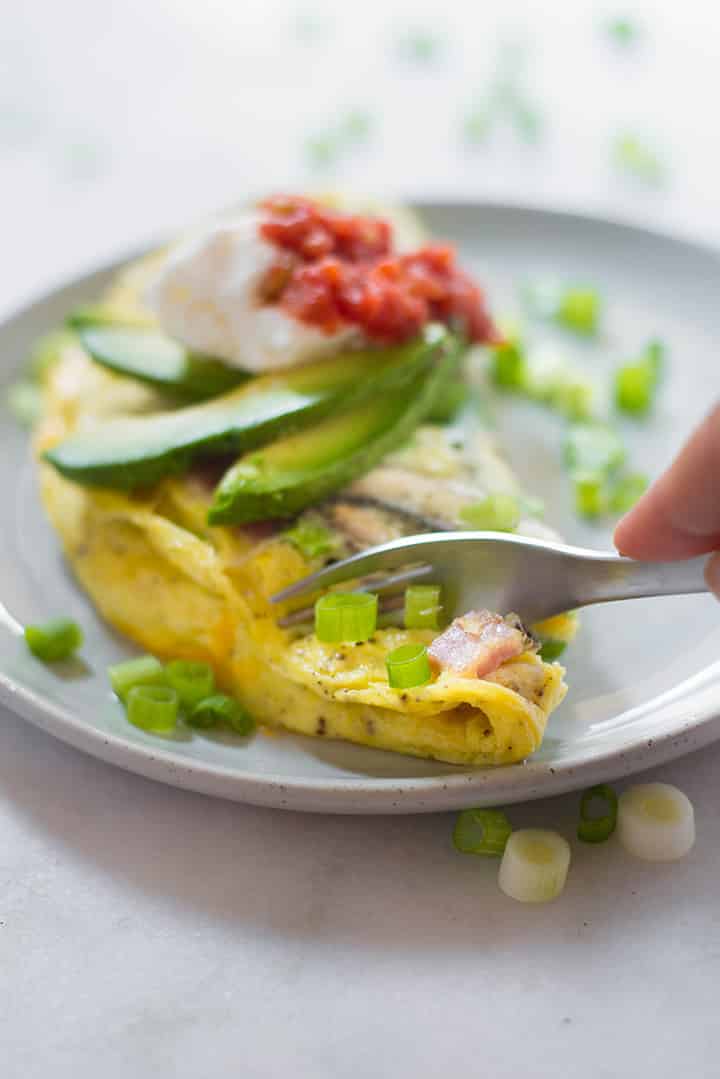 A close up side view of the omelet and someone with a fork in hand digging into the omelet.