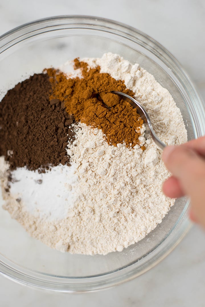Mixing bowl filled with the dry ingredients needed for the Healthy Chocolate Zucchini Bread including coconut sugar, flour, cinnamon, cocoa powder, and baking powder.