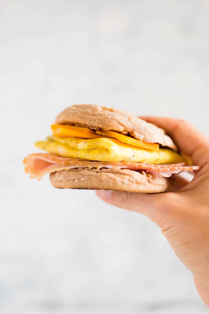 Close up of a hand holding one breakfast sandwich.