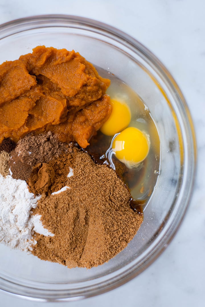 Close up of a mixing bowl filled with pumpkin bread ingredients including spelt flour, eggs, pumpkin puree, coconut sugar, coconut oil, ground cinnamon, ground nutmeg, ground ginger, ground all spice, sea salt, baking powder, and baking soda.