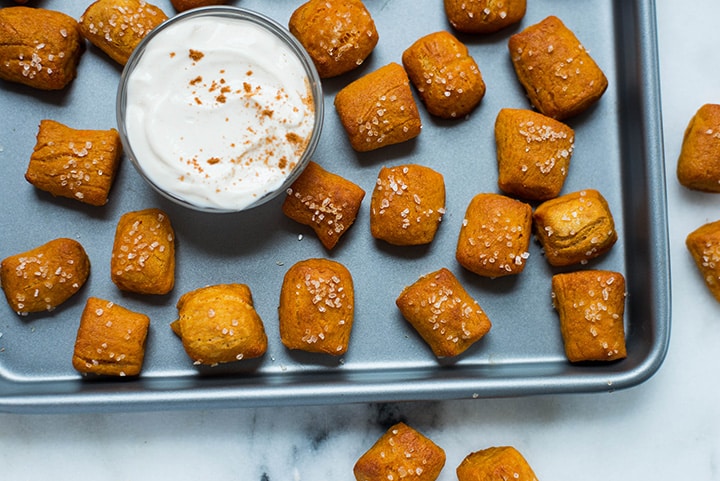 Soft Pretzel Bites with Sweet Potato Dough on a baking trey with the sweet yogurt-based dipping sauce in the middle and a few pretzel bites on the table.