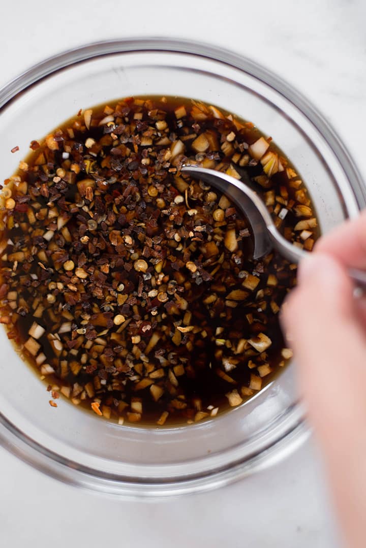 Close up of a mixing bowl that contains a mixing bowl with honey, garlic, soy sauce, ginger, rice vinegar, and crushed red pepper flakes mixed together.
