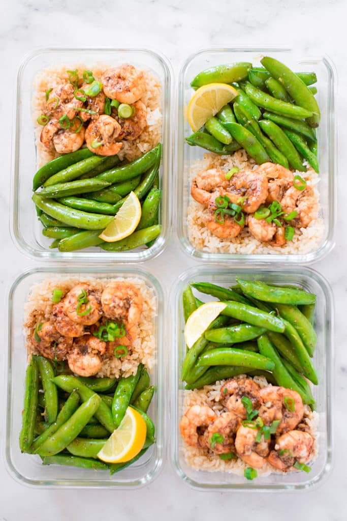 view from above of 4 meal prep containers that contain shrimp, brown rice, sweet peas, and lemon slices.