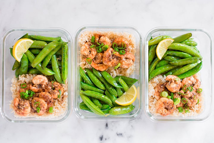View from the top of 3 meal prep containers filled with shrimp, sweet peas, rice. A lemon slice was added in all the meal prep containers.