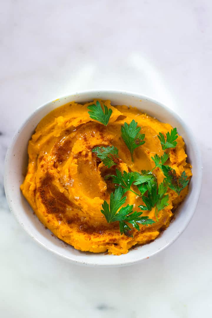Overhead image of Healthy Sweet Potato Hummus garnished with parsley, paprika, and olive oil in a serving bowl.